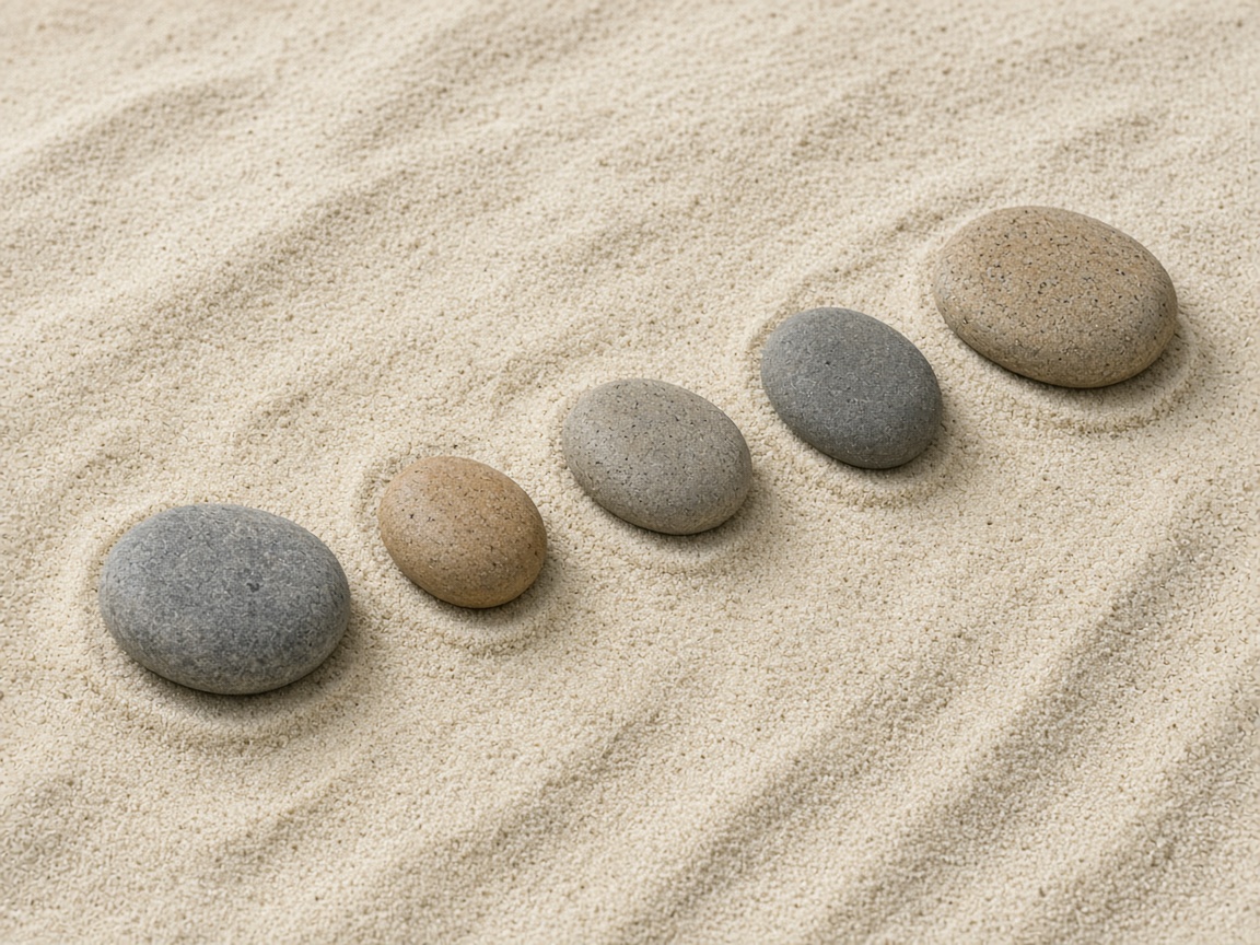 Five smooth stones form a gentle curve on sand.