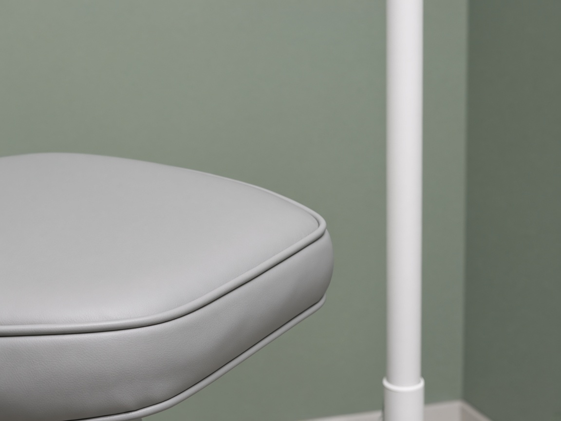 A close view of a light-gray dental chair cushion beside a smooth white light pole against a sage wall.