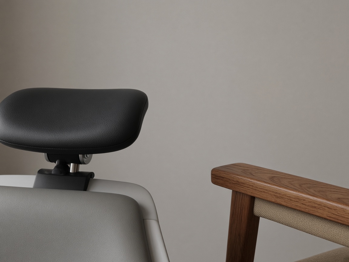 A close view of a black chair headrest next to a wood armrest on a warm gray wall.