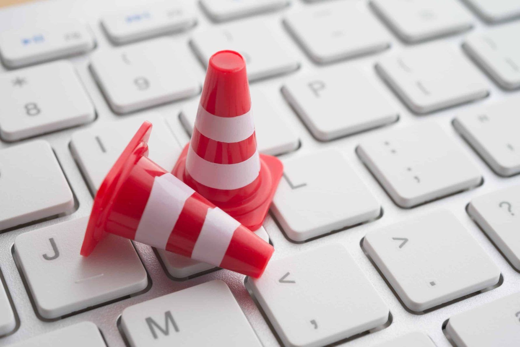 Two small red and white traffic cones on a computer keyboard, symbolizing website maintenance and technical support.